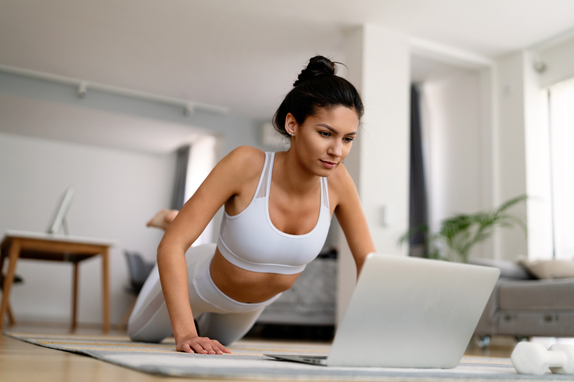 Young fit woman in sportswear watching online video with fitness exercises on laptop